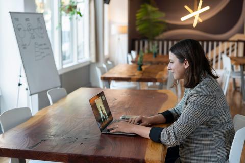 A woman in a jacket sits at a desk with her laptop in a video call. 